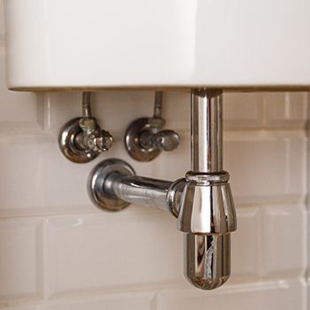 Silver pipes underneath a sink that may be repaired or replaced during a bathroom remodel.