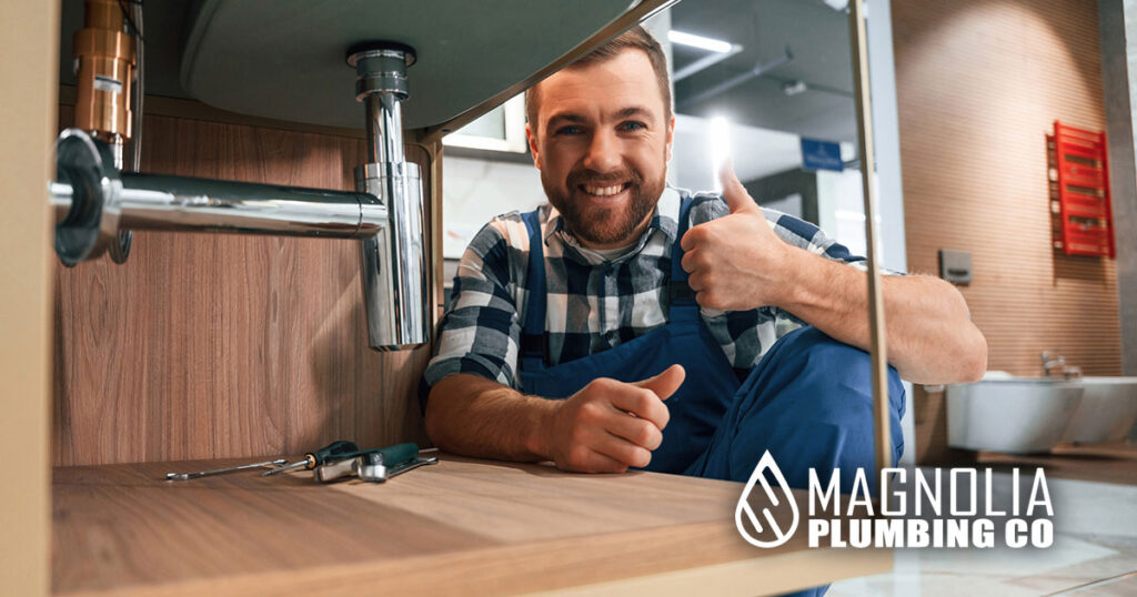 Showing thumb up and smiling. Plumber in blue uniform is at work in the bathroom indicating Memphis plumbing problem solved.