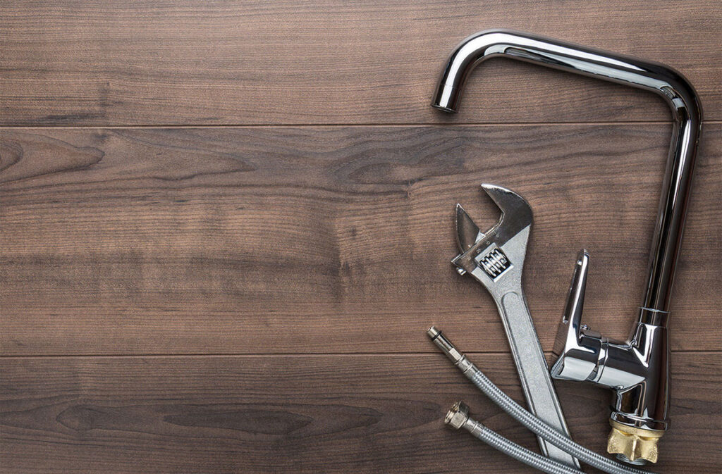 sink faucet, wrench and water line on a dark wood floor